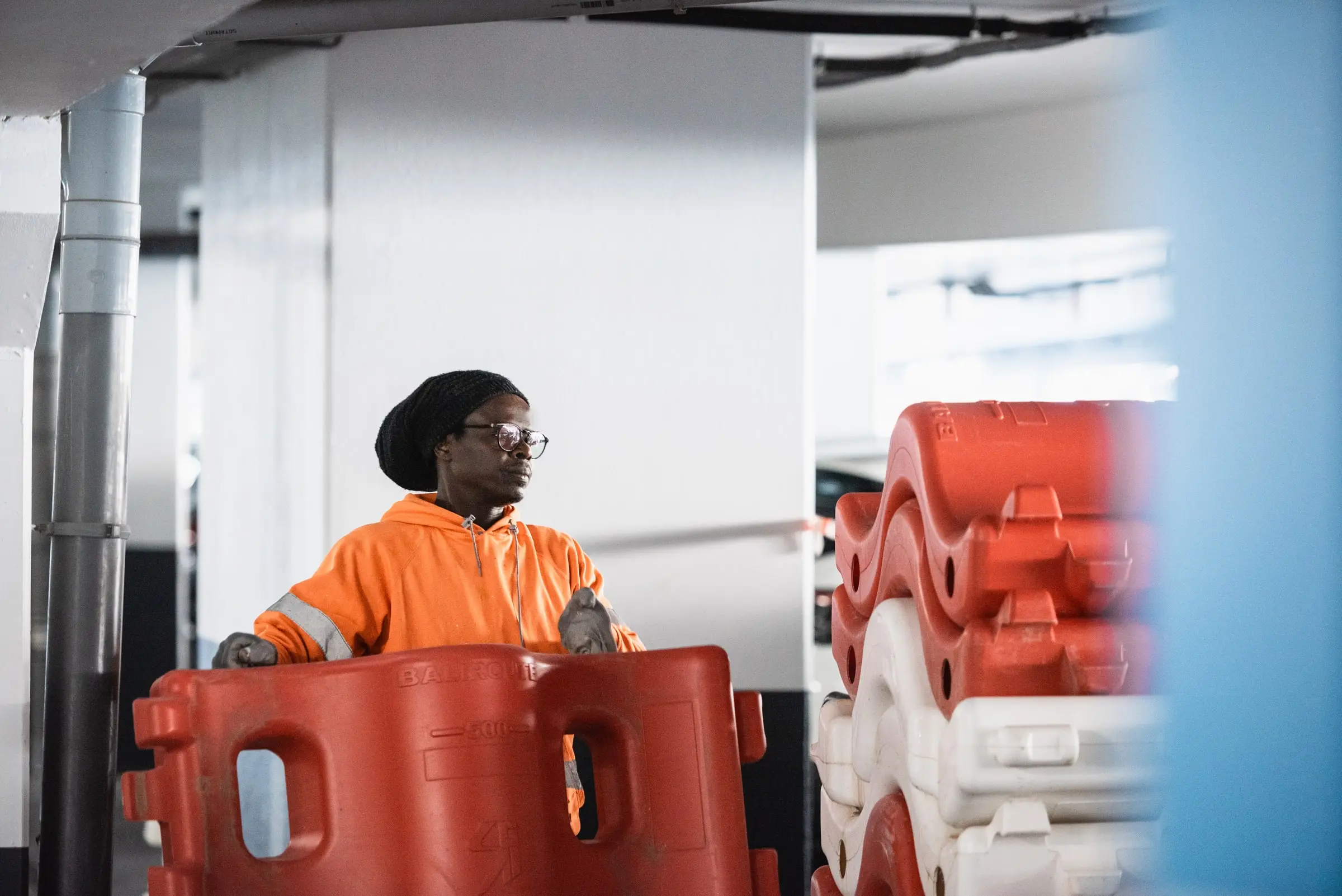 Salarié ASM en gilet orange déplaçant une barrière modulaire rouge dans un parking