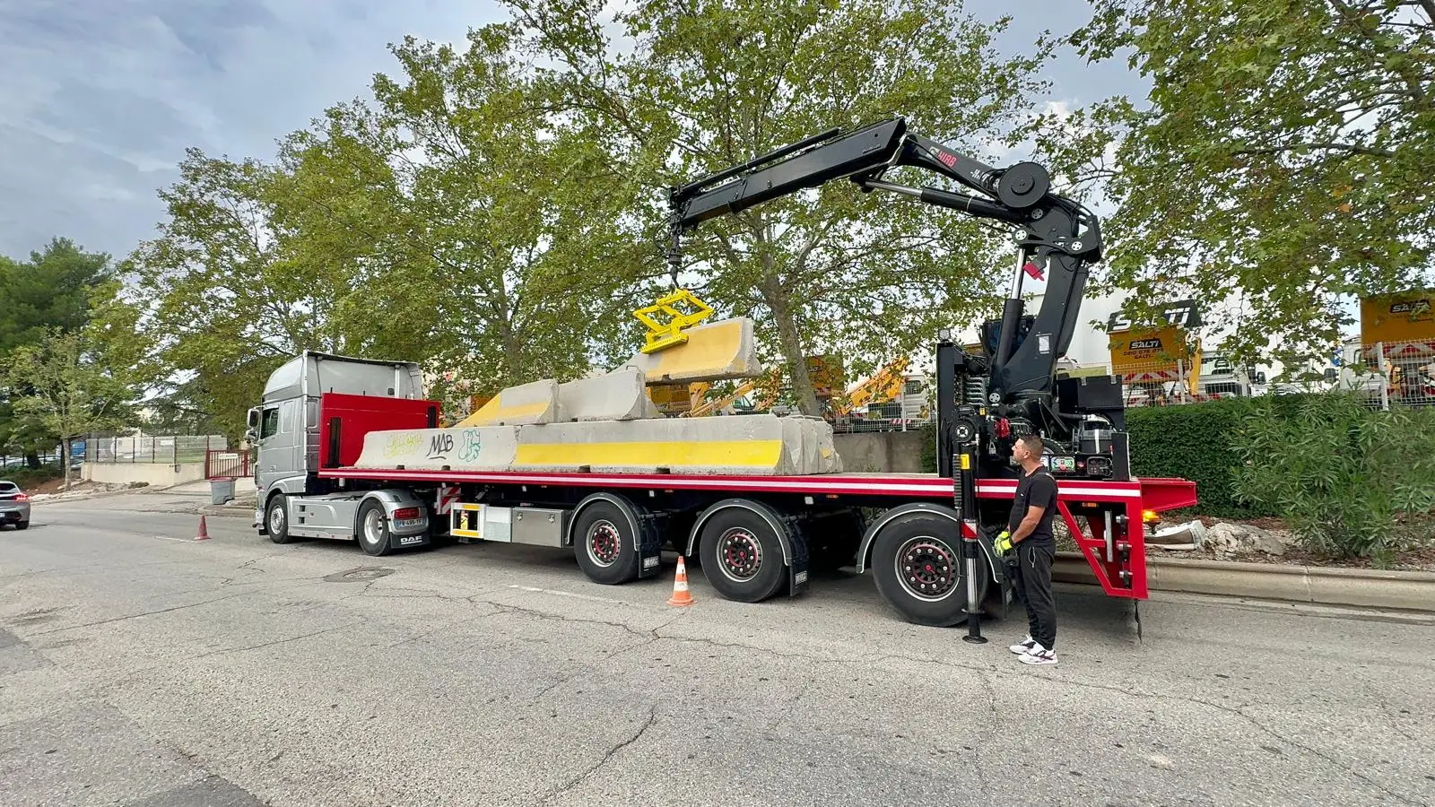 Camion-grue ASM chargé de séparateurs béton jaune et blanc, stationné le long d’une voie