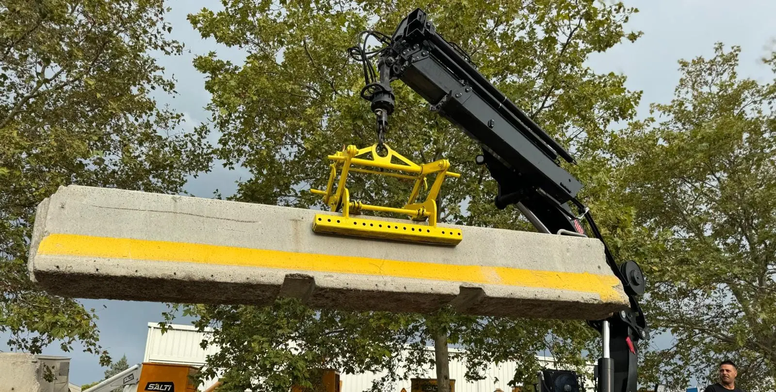 Pince de levage jaune saisissant un séparateur béton sous la grue