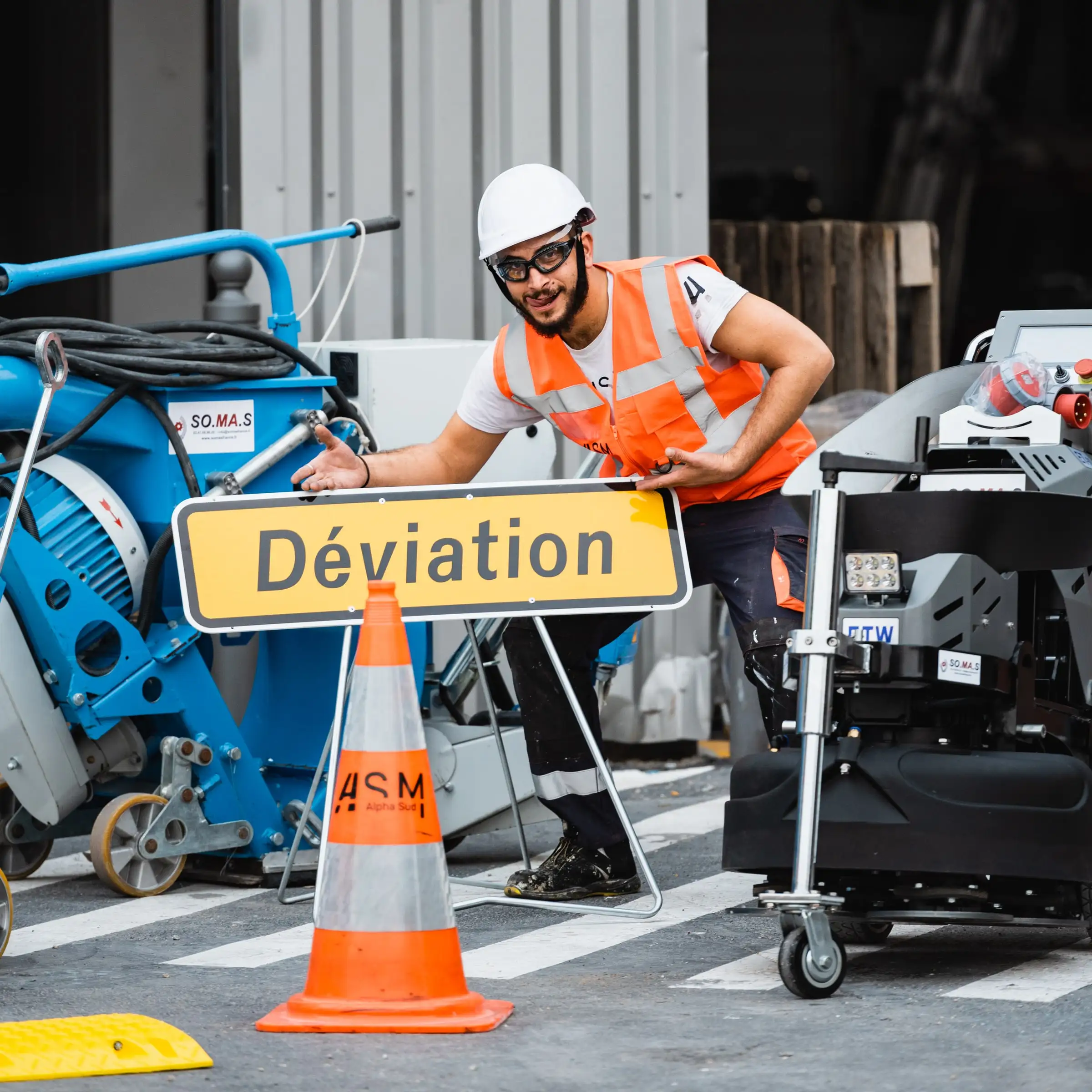 Salarié ASM en gilet orange et casque posant un panneau « Déviation » à côté d’un cône sur un passage piéton