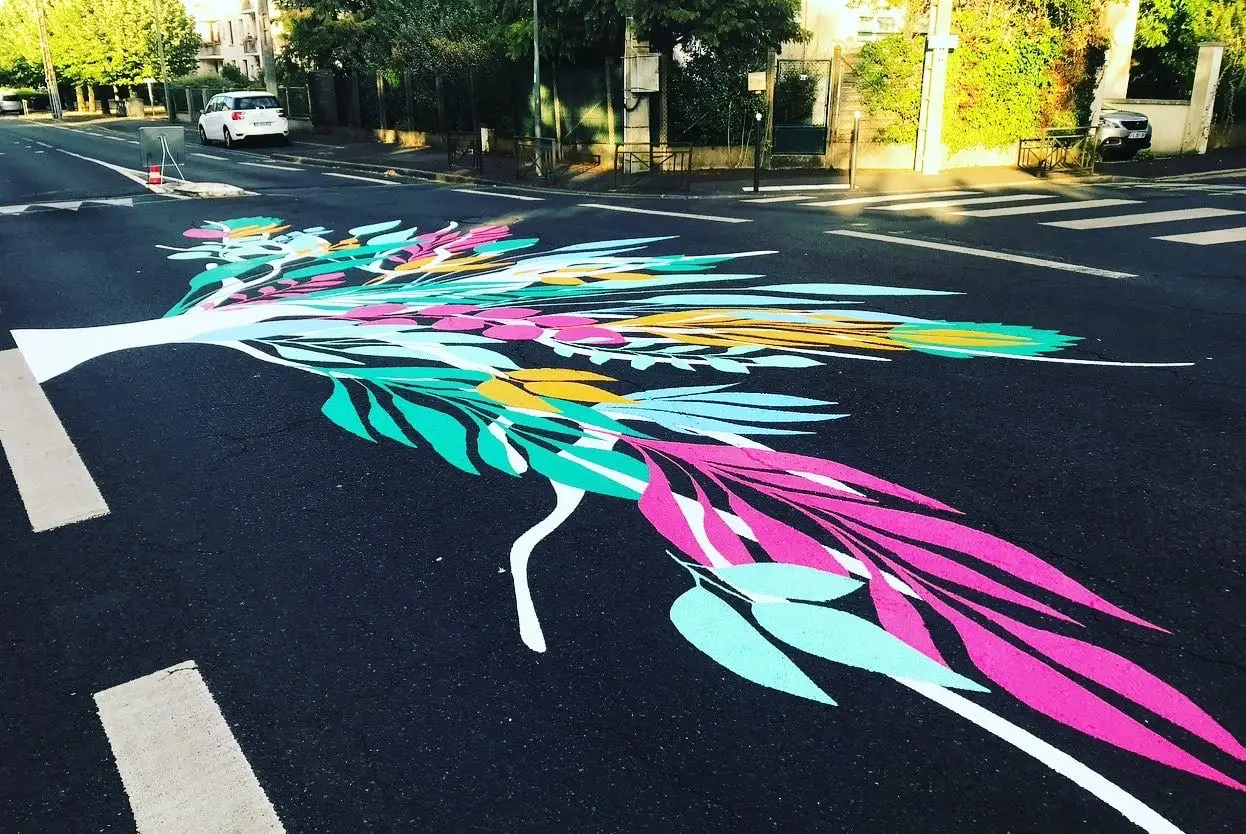 Envol de feuillages roses, verts et jaunes peint à même l’enrobé d’une chaussée