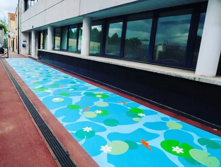 Cheminement peint en décor de nénuphars bleus et verts le long d’un bâtiment