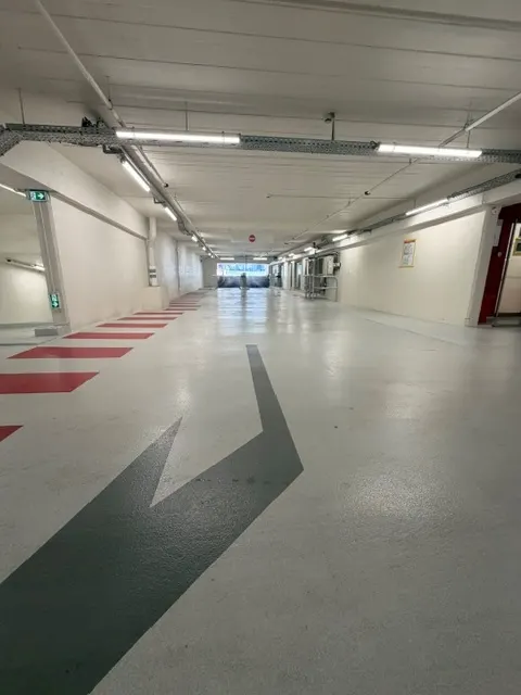 Cheminement piéton rouge et flèche de sens de circulation menant vers la sortie du parking
