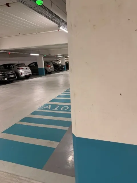 Secteur de parking repéré par une couleur : allée piétonne et soubassement de pilier bleus, numéro de place peint au sol