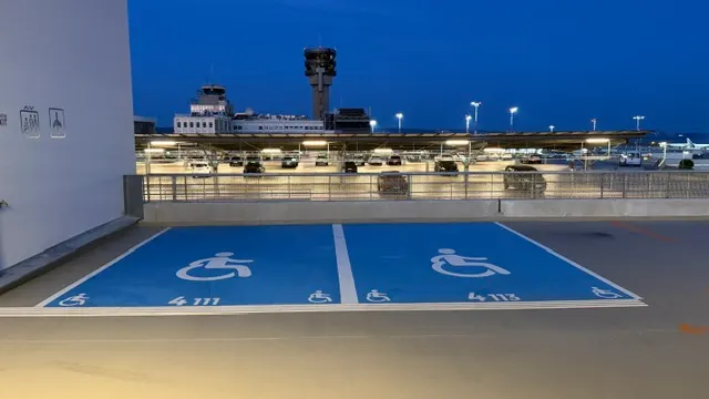 Places PMR peintes en bleu sur un niveau de parking de l’aéroport, terminal éclairé à l’arrière-plan