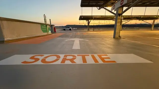 Niveau en toiture d’un parking de l’aéroport Marseille Provence au crépuscule, « SORTIE » peint en orange sur toute la largeur de l’allée
