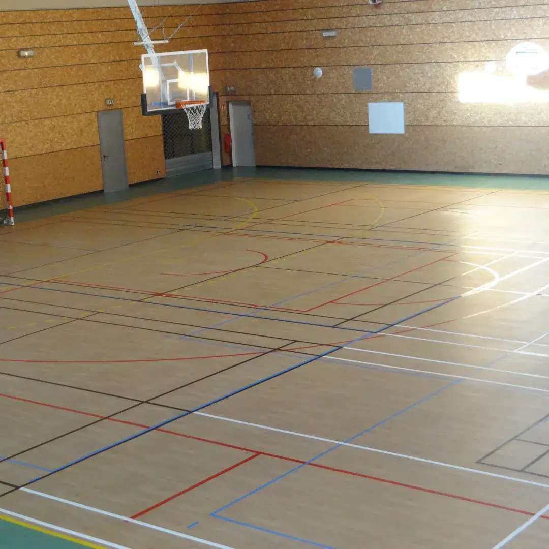 Sol de gymnase portant les tracés superposés de plusieurs sports en couleurs distinctes