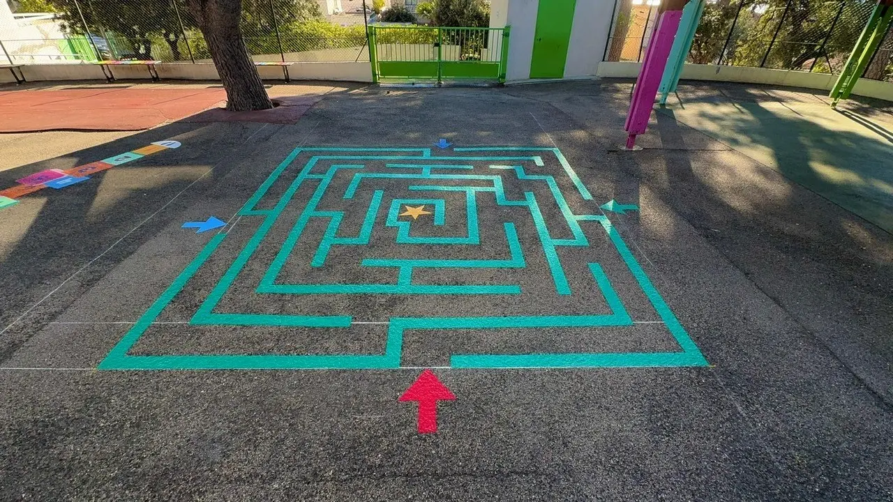 Grand labyrinthe vert tracé au sol d’une cour d’école, flèches de départ colorées