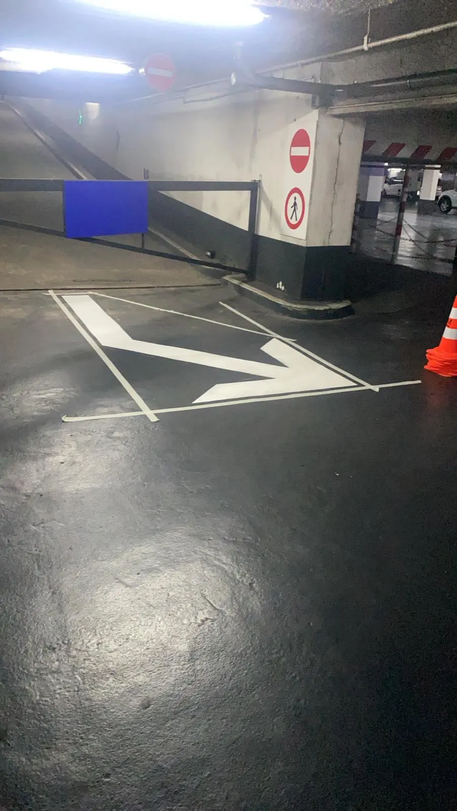 Grande flèche directionnelle blanche cernée de noir, tracée au sol devant une barrière du parc