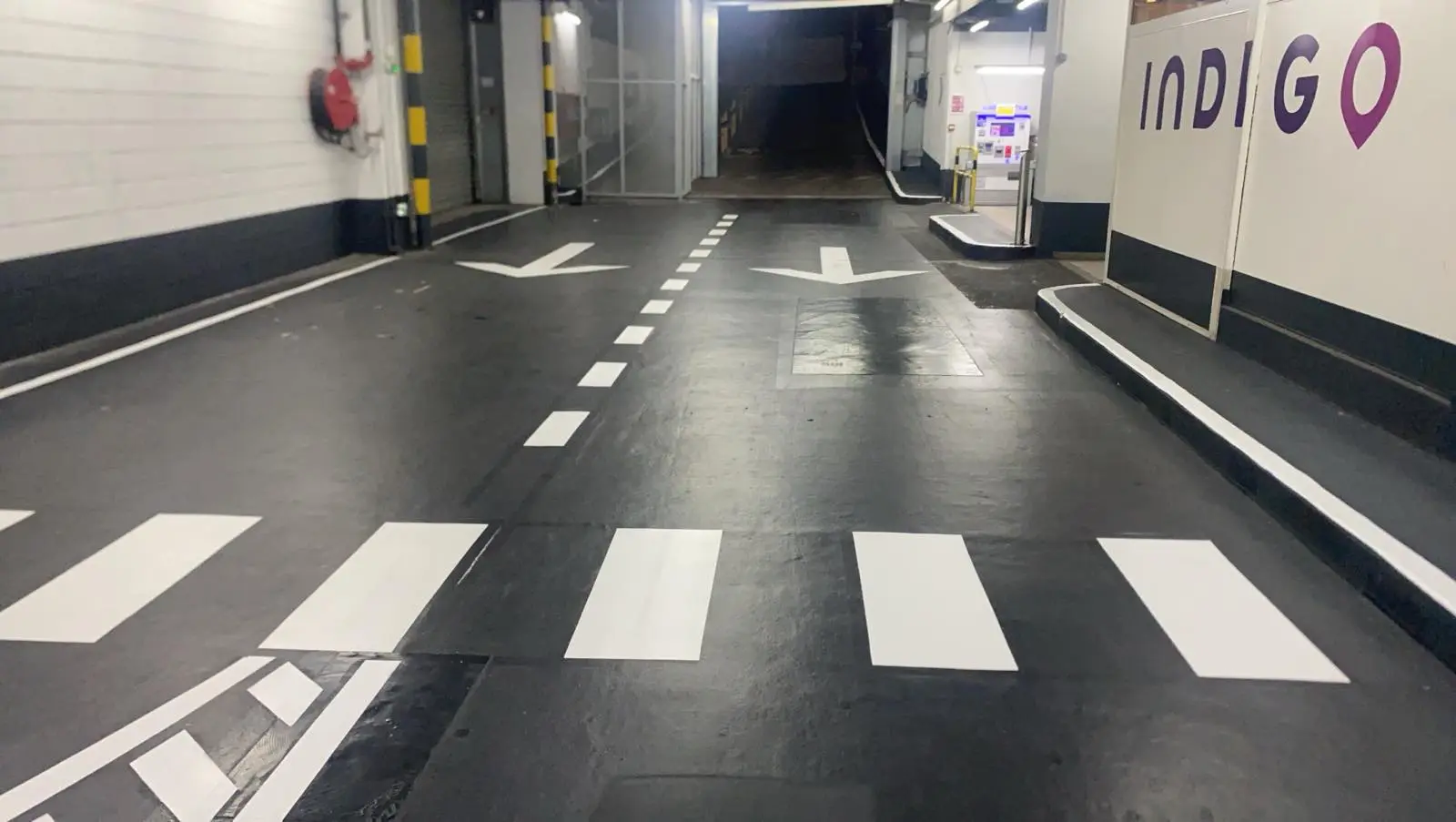 Flèches de circulation blanches tracées au sol dans une voie de parking en ouvrage