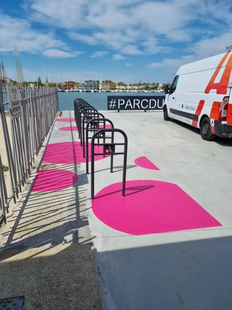 Zone de stationnement vélos peinte en rose vif le long d’un bâtiment