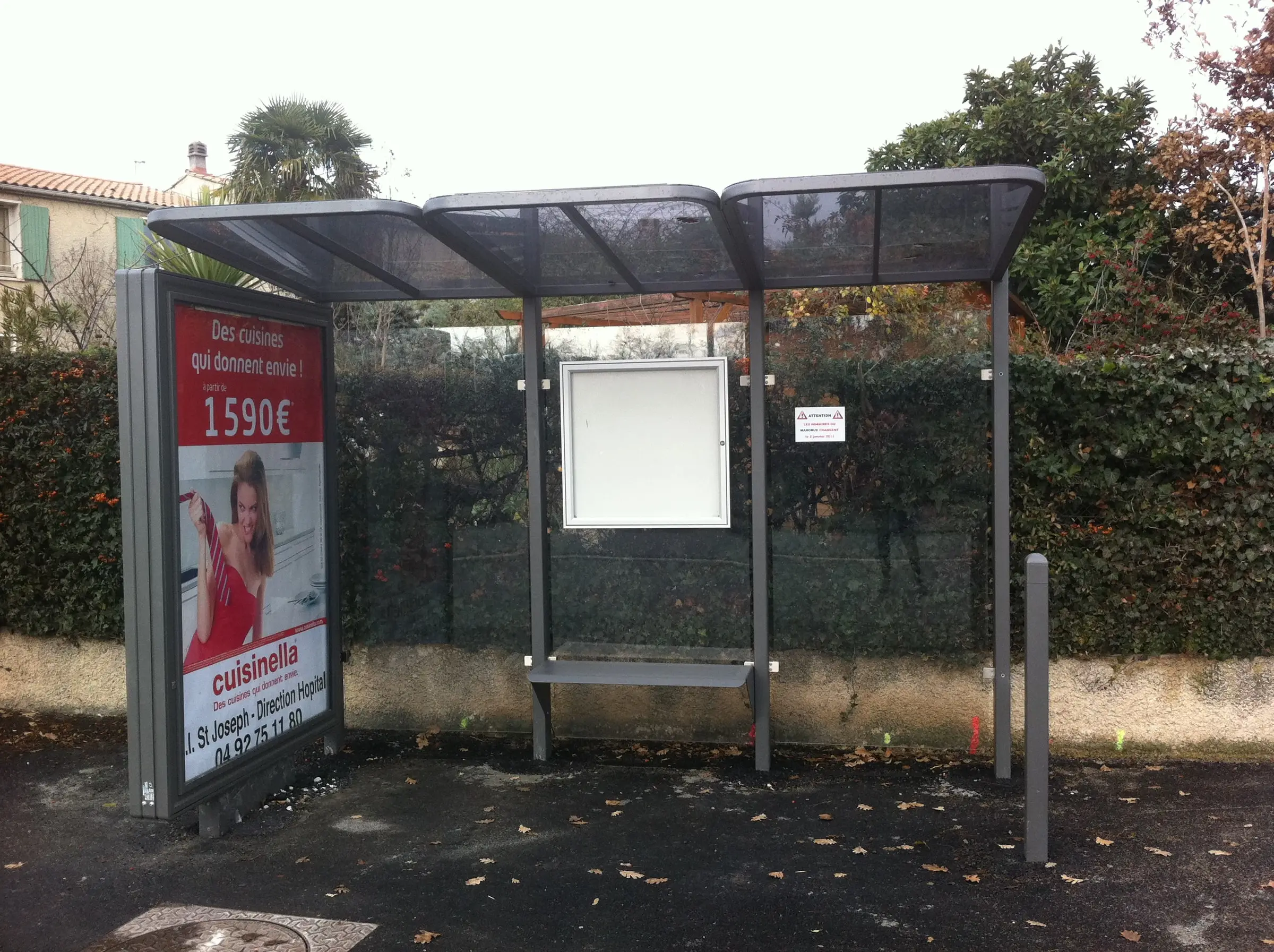 Abri bus vitré à toit incurvé et caisson d’affichage, installé le long d’une rue