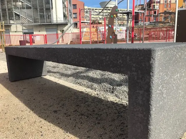 Banc monobloc en béton désactivé posé sur un parvis, ville en arrière-plan