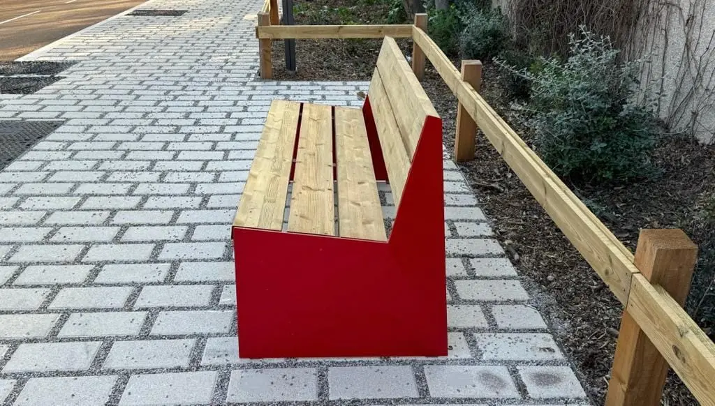 Banc bois et acier rouge posé sur un cheminement pavé