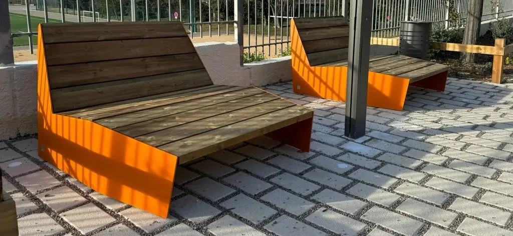 Bancs à assise bois et flancs orange installés sur un parvis pavé