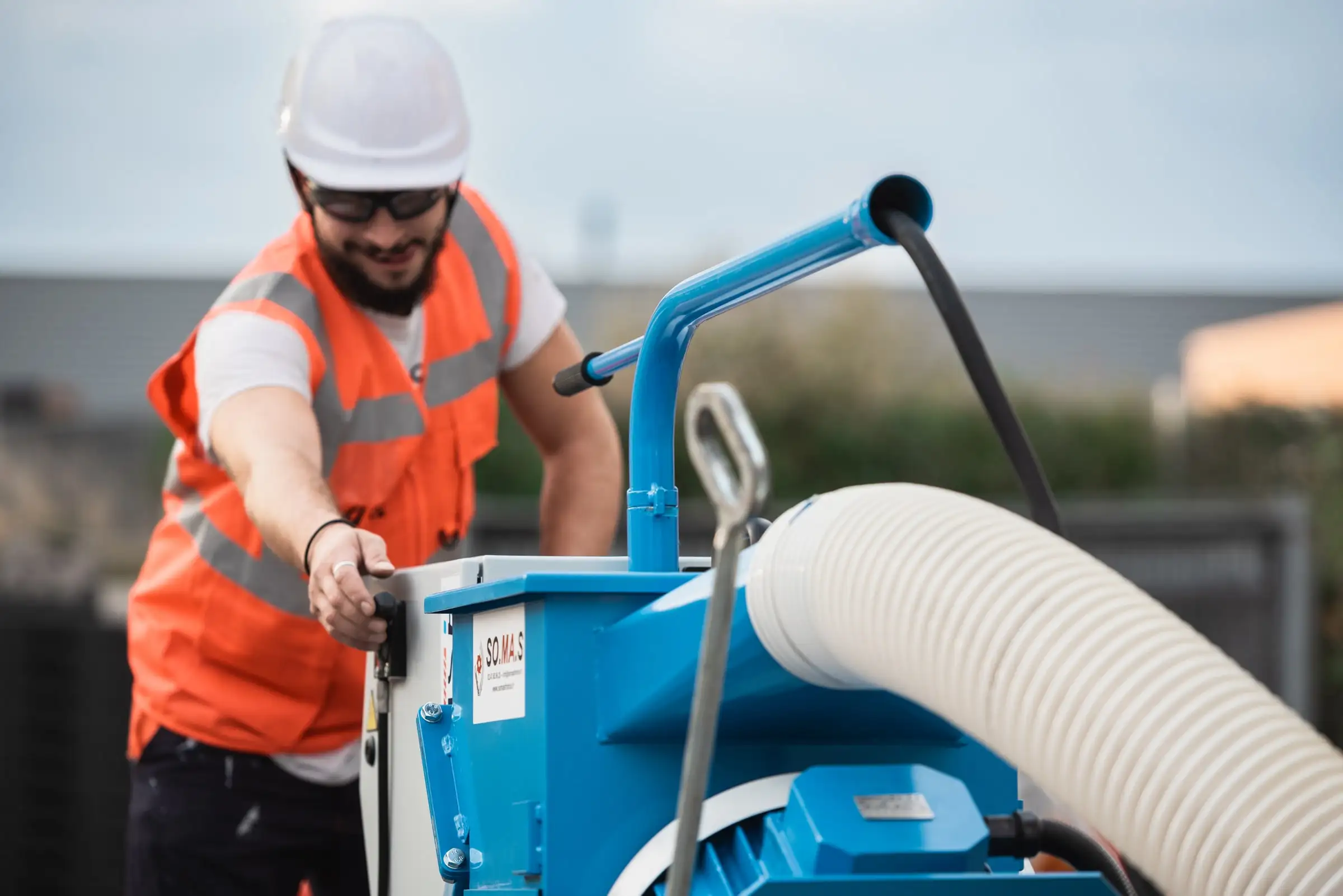 Technicien ASM en gilet orange et casque manœuvrant une grenailleuse sur un chantier au bord de la mer