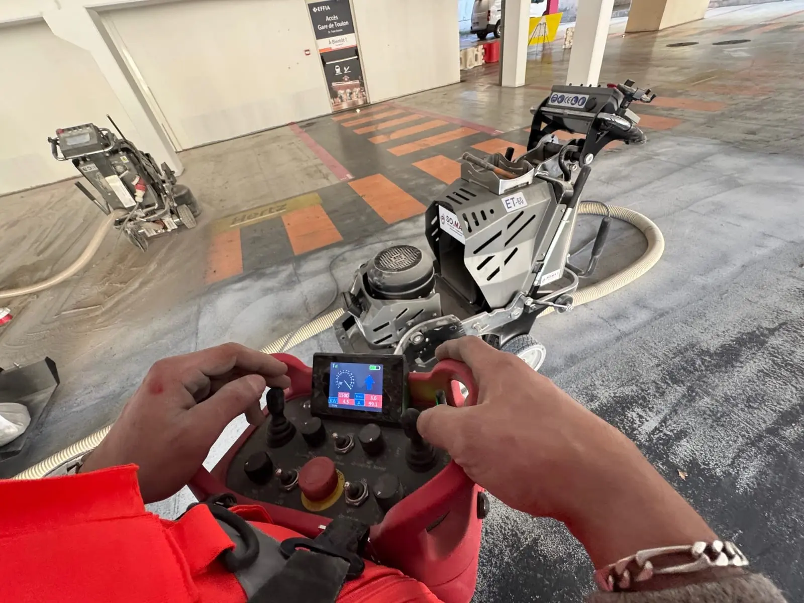 Mains d’un opérateur ASM sur la commande d’une ponceuse de sol, en parking