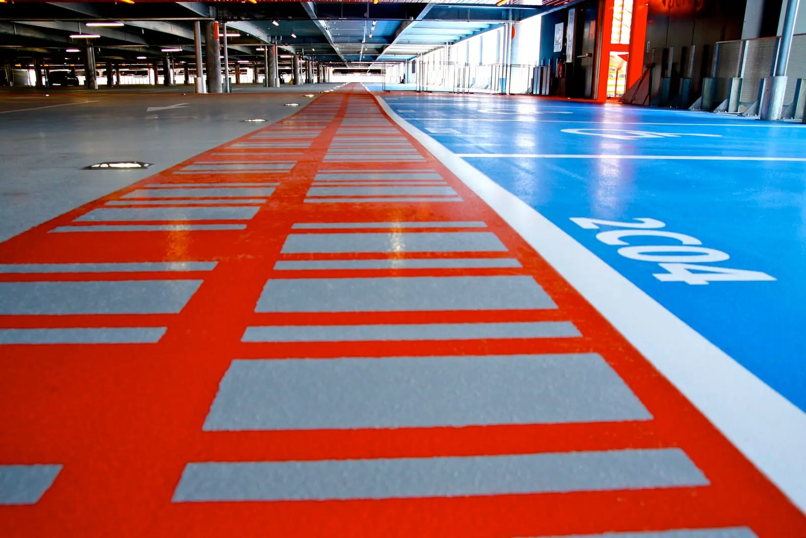 Chemin piéton rouge et place PMR bleue en résine sur un niveau du parking de l’aéroport Toulouse-Blagnac