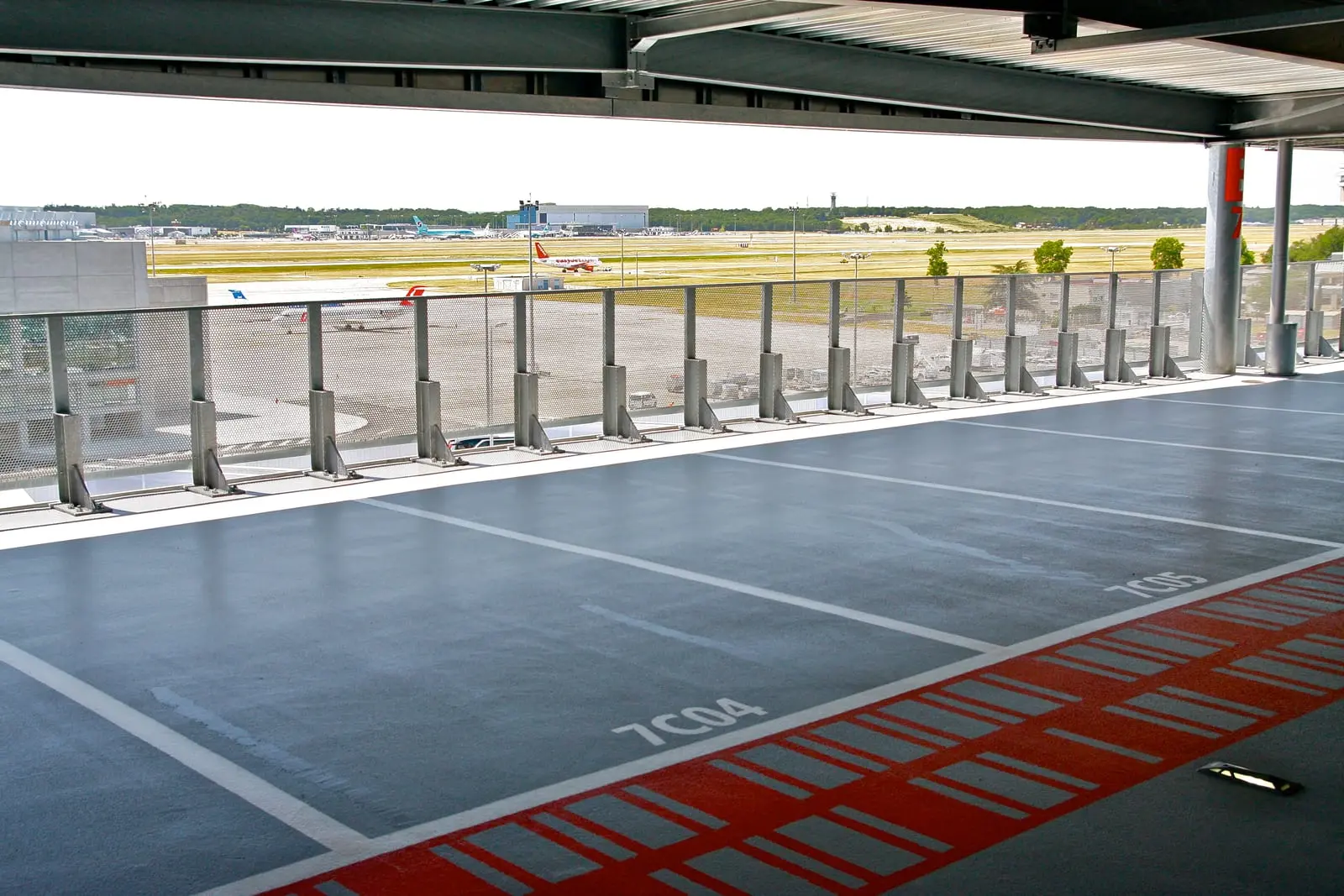 Niveau de parking résiné gris ouvert sur les pistes de l’aéroport Toulouse-Blagnac, cheminement rouge en pied de places