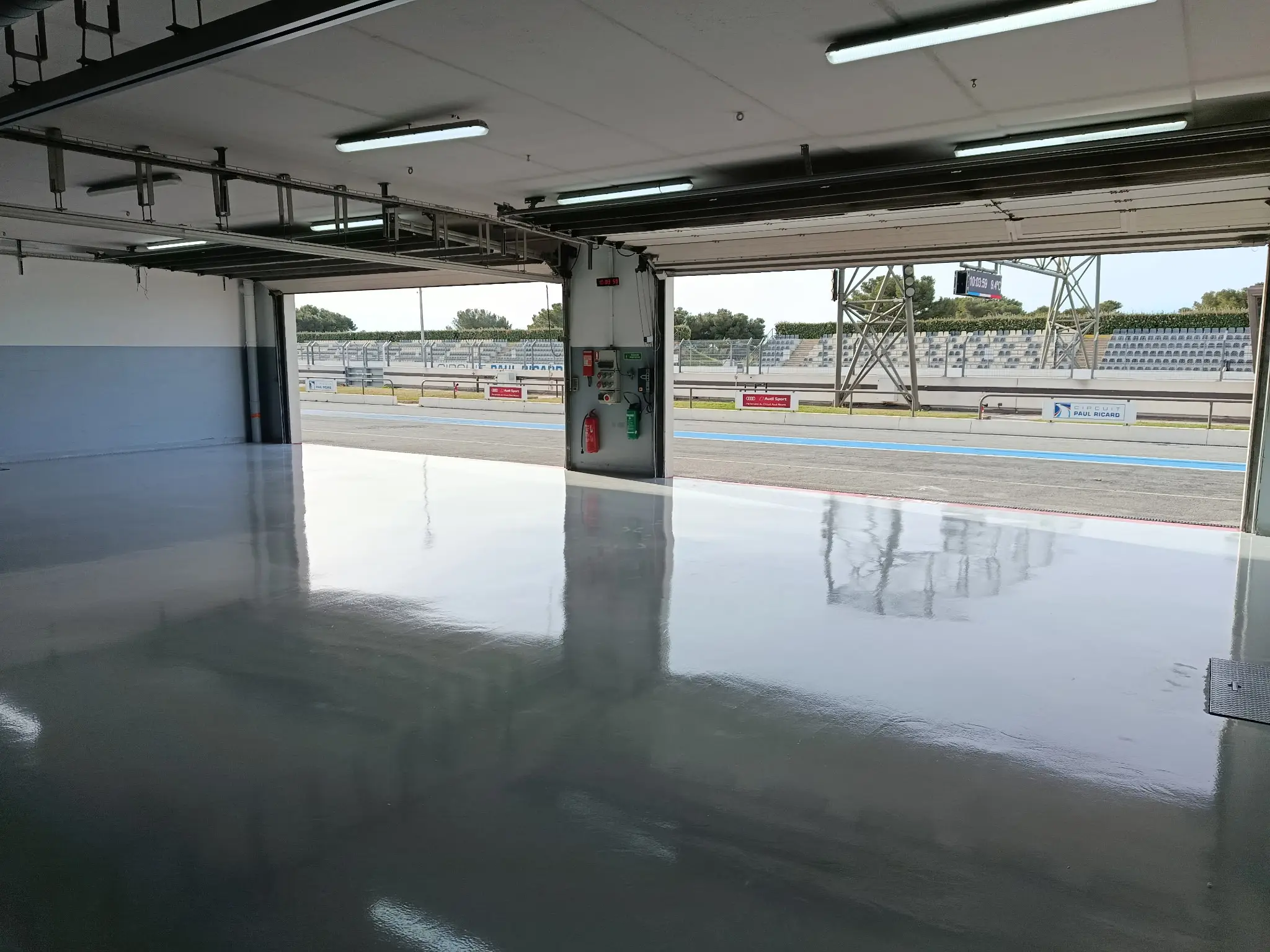 Box du Circuit Paul Ricard au sol résine reflétant les néons, ouvert sur la piste