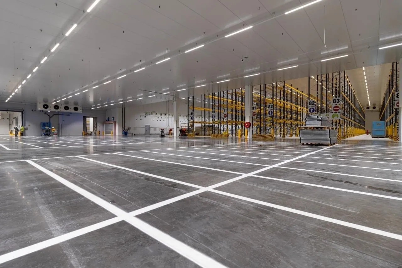 Entrepôt logistique neuf, sol résine gris et marquage blanc quadrillant les zones de stockage devant les racks jaunes