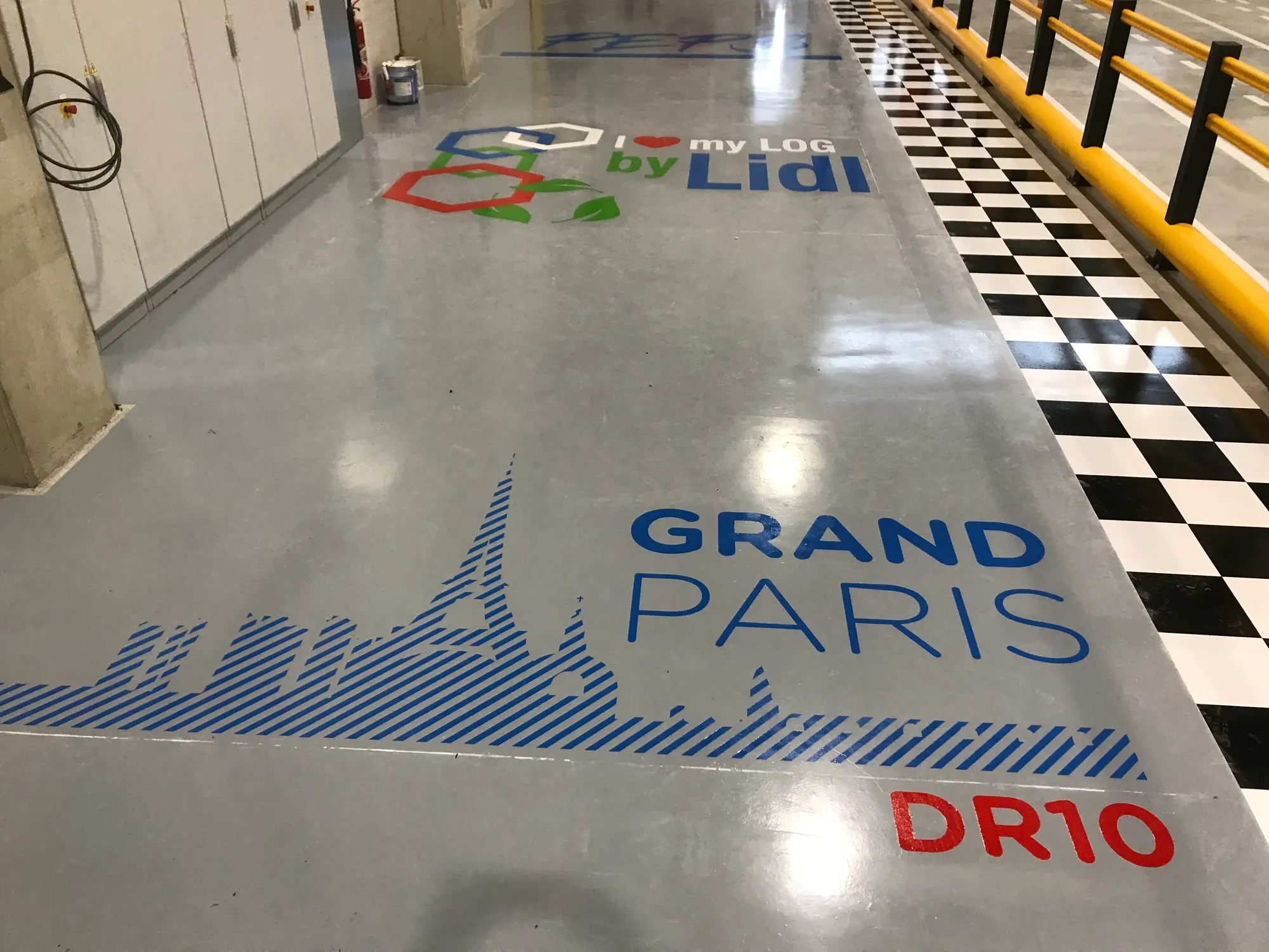 Sol résiné d’une plateforme Lidl Grand Paris : logo « I love my LOG by Lidl », silhouette de Paris et damier noir et blanc en rive de circulation