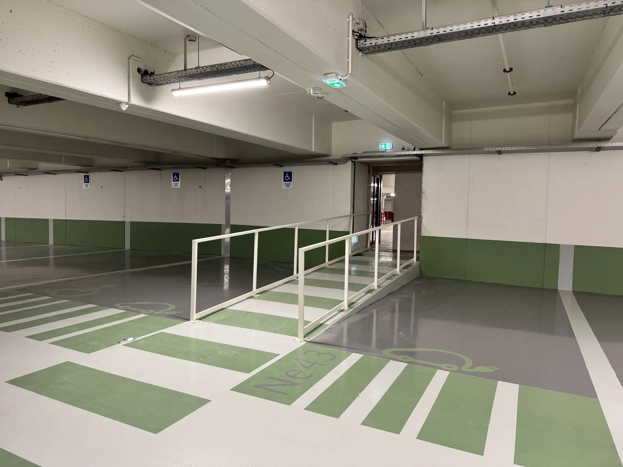 Niveau du parking du Diamant à Ajaccio : places électriques et places PMR sur résine verte, cheminement piéton protégé par un garde-corps