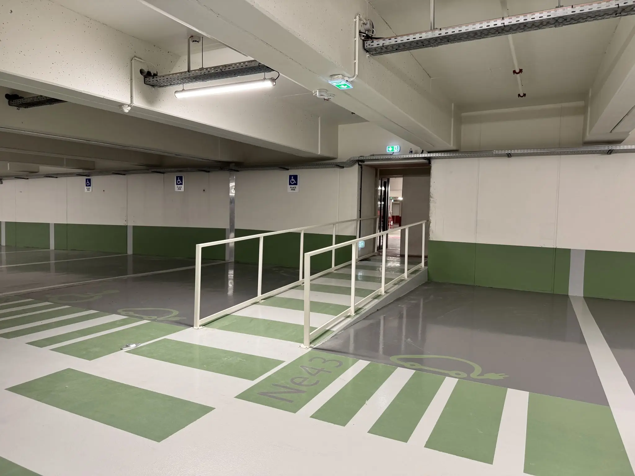 Niveau du parking du Diamant à Ajaccio : places électriques et places PMR sur résine verte, cheminement piéton protégé par un garde-corps