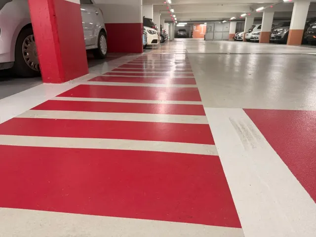 Cheminement piéton rouge du parking du Diamant, bandes en épi sur résine gris clair
