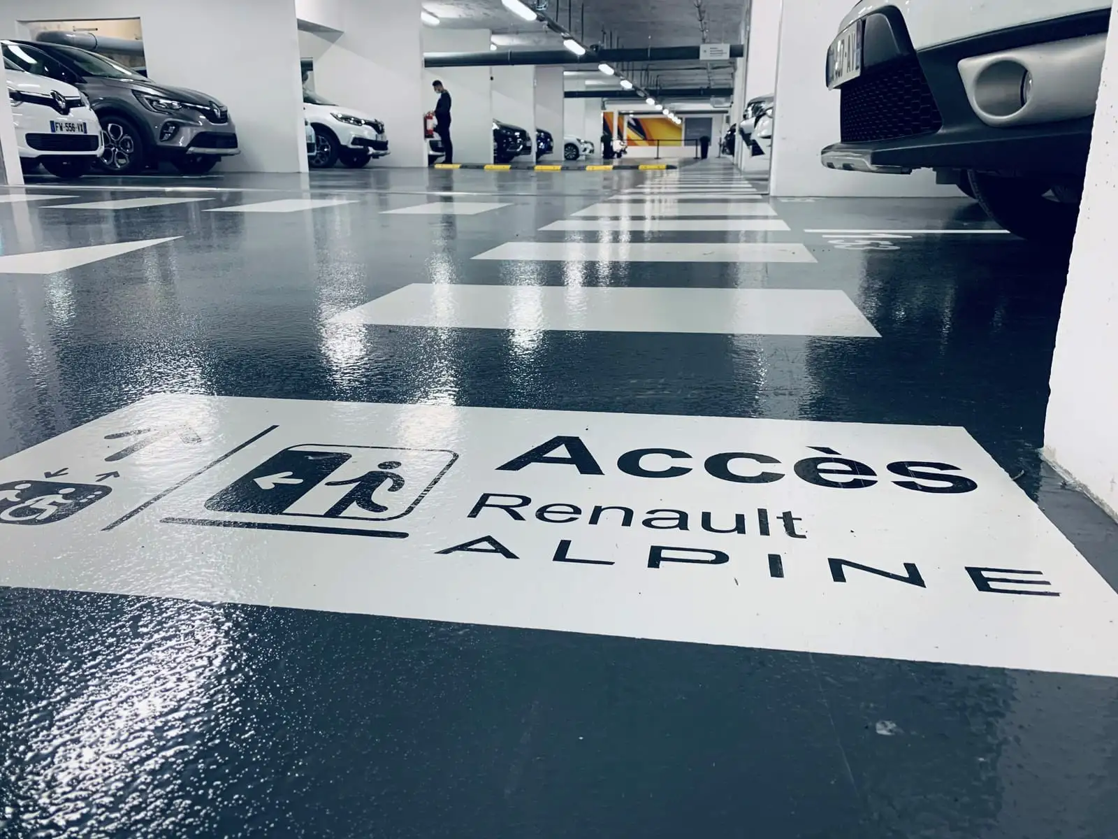 Sol de parking résiné du showroom Renault, marquage « Accès Renault ALPINE » et traversée piétonne au premier plan