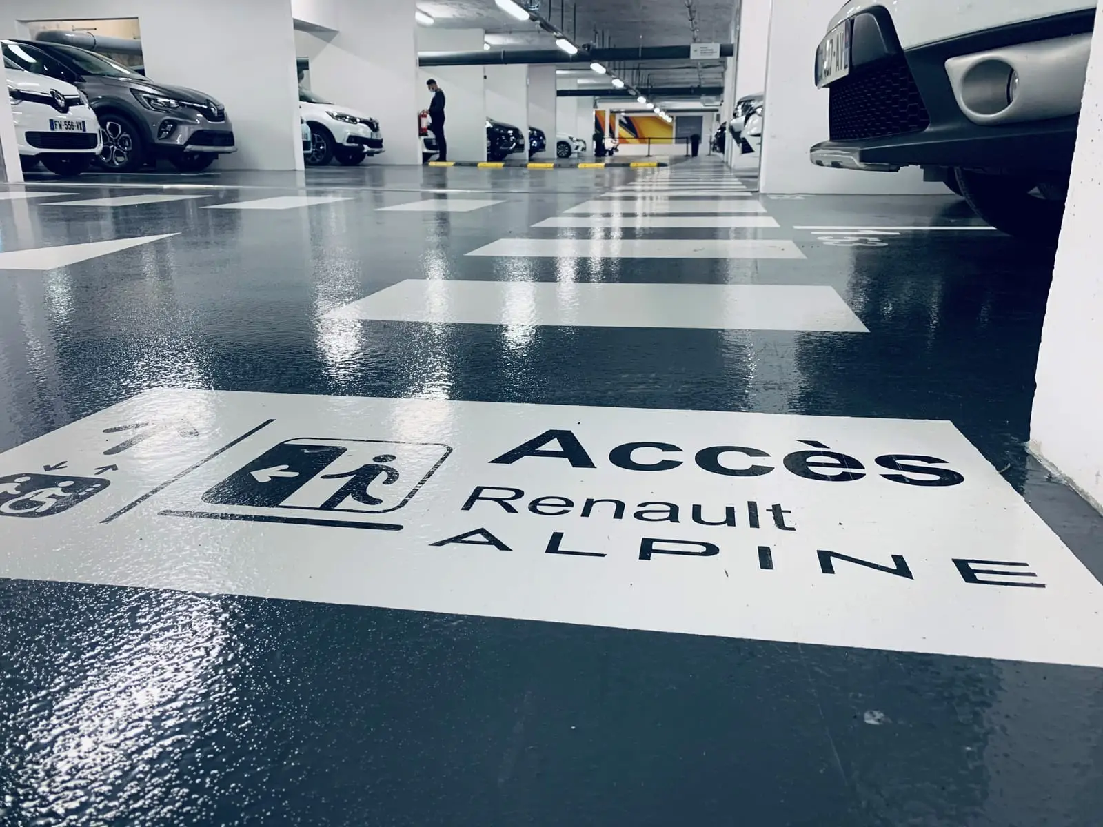 Sol de parking résiné du showroom Renault, marquage « Accès Renault ALPINE » et traversée piétonne au premier plan