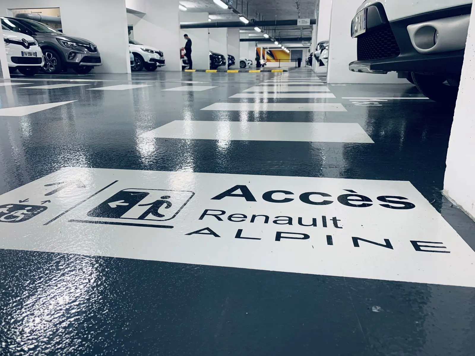 Marquage au sol « Accès Renault ALPINE » avec pictogramme d’ascenseur, sur la résine du parking du showroom