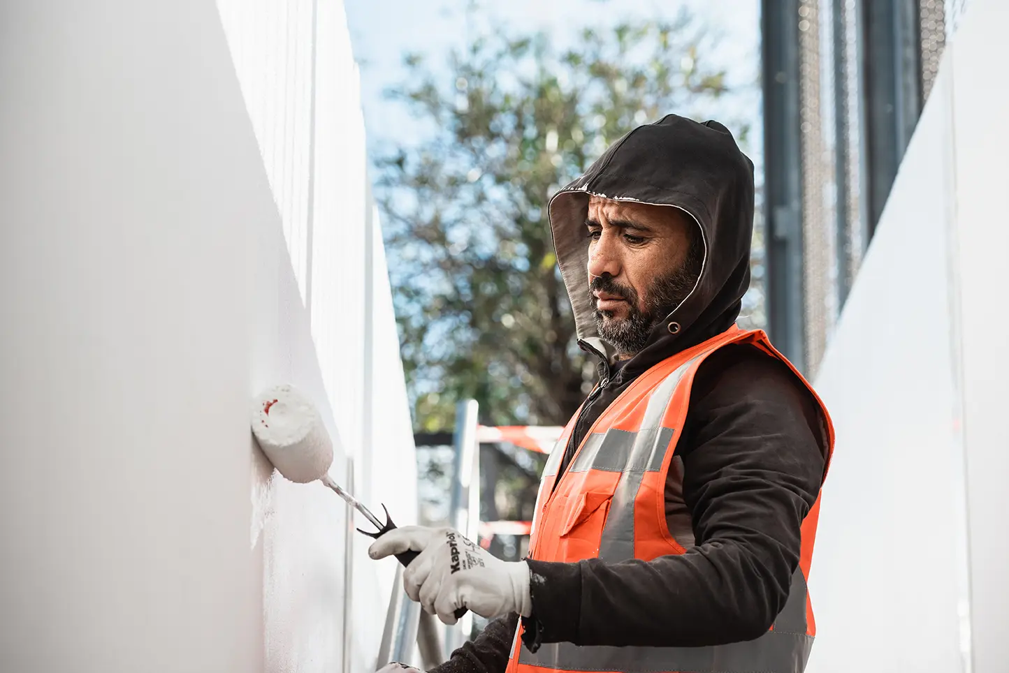 Applicateur ASM peignant au rouleau le mur blanc d’un bâtiment, gilet haute visibilité