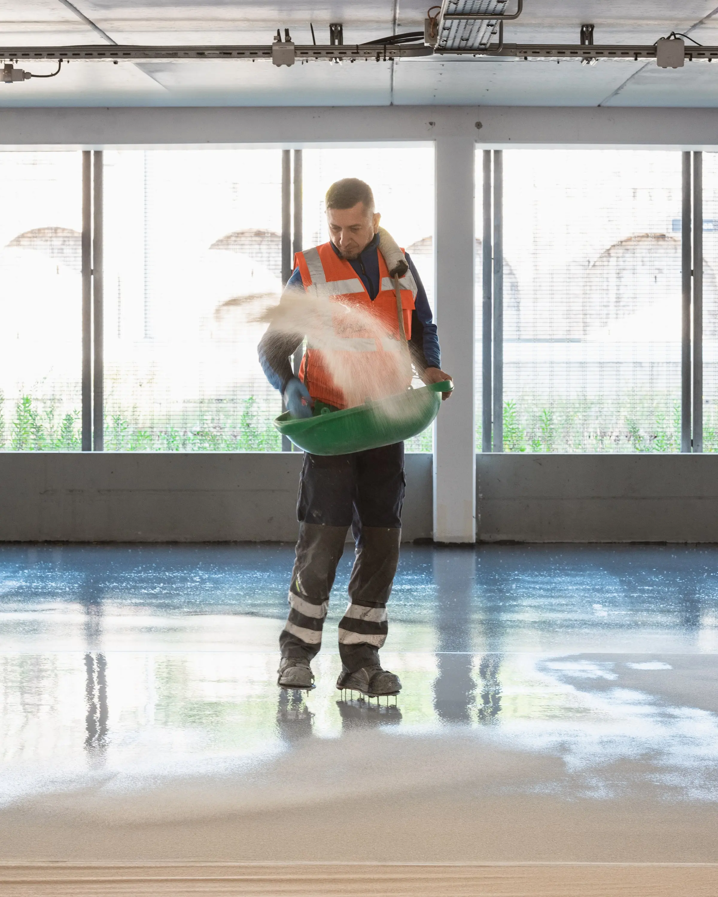 Applicateur ASM projetant du quartz coloré sur une résine de sol fraîche dans un parking