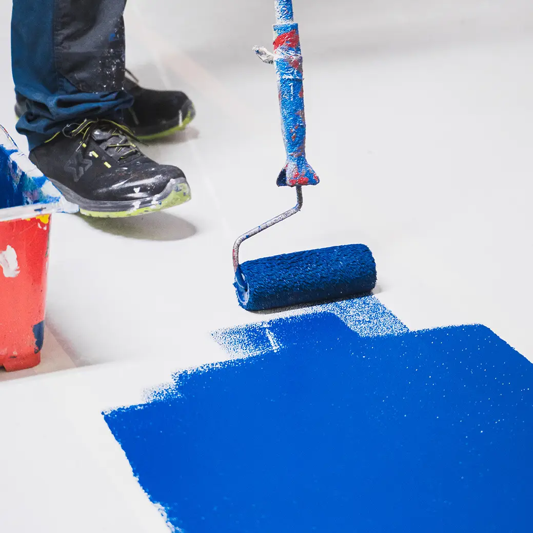 Salarié ASM appliquant au rouleau une résine bleue sur un sol de parking