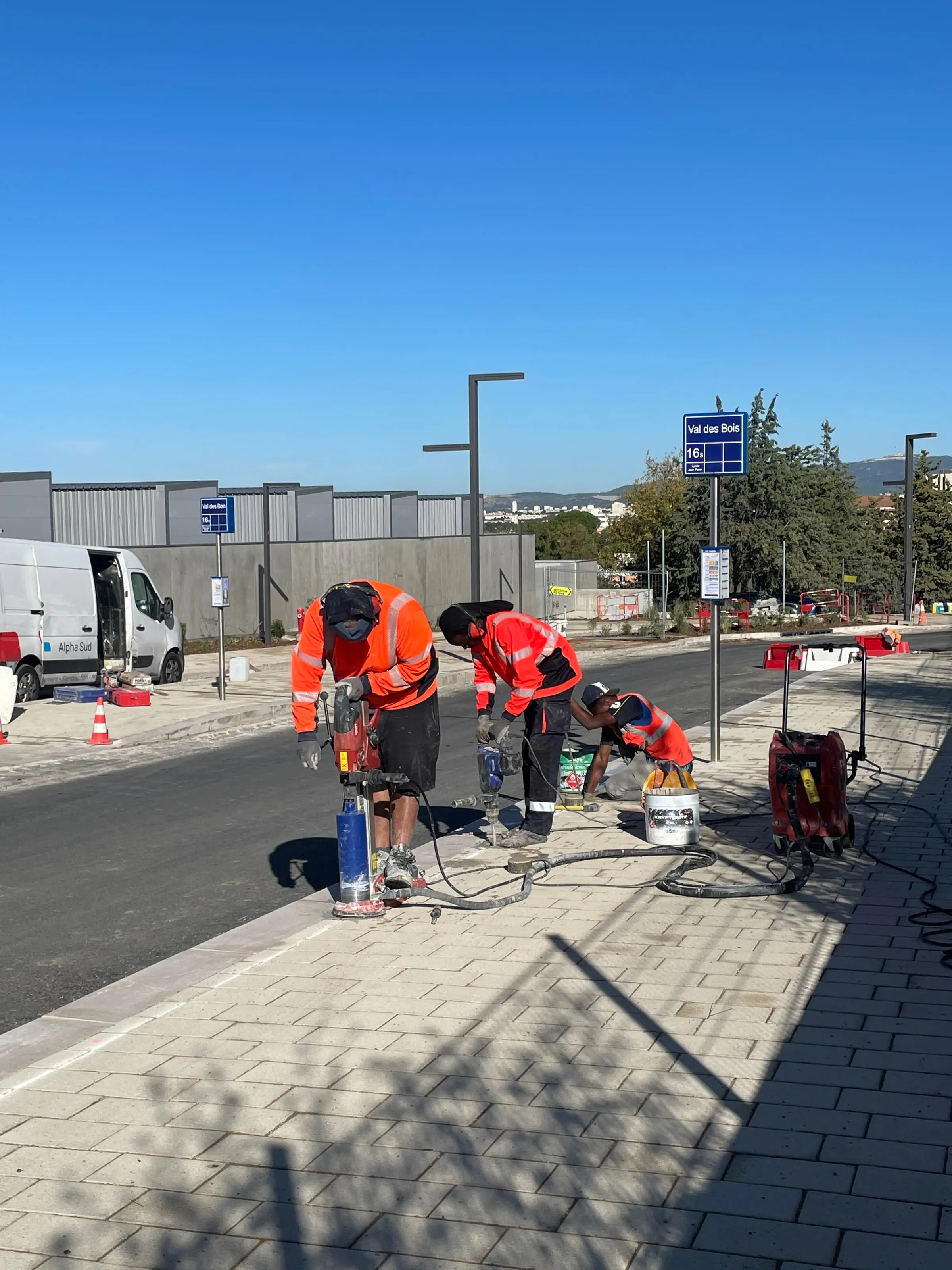 Équipe ASM carottant un trottoir pour sécuriser une voirie, fourgons stationnés à l’arrière