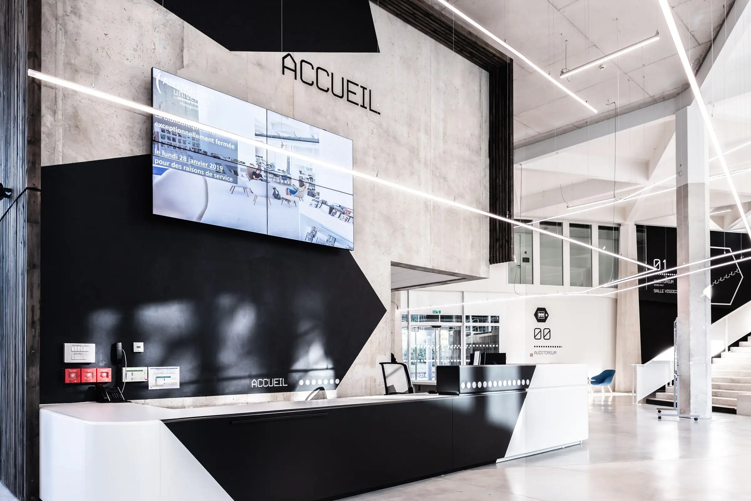 Hall d’accueil habillé d’une signalétique murale contemporaine, banque « Accueil » et écran d’information