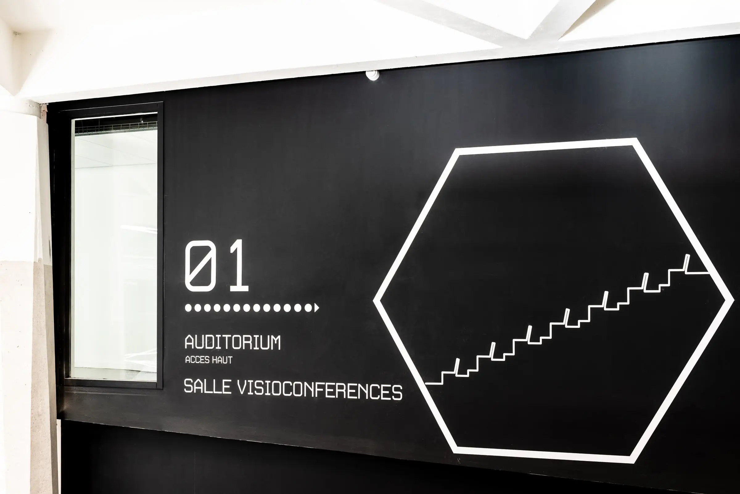 Signalétique directionnelle « Auditorium » tracée en filet lumineux sur un mur noir
