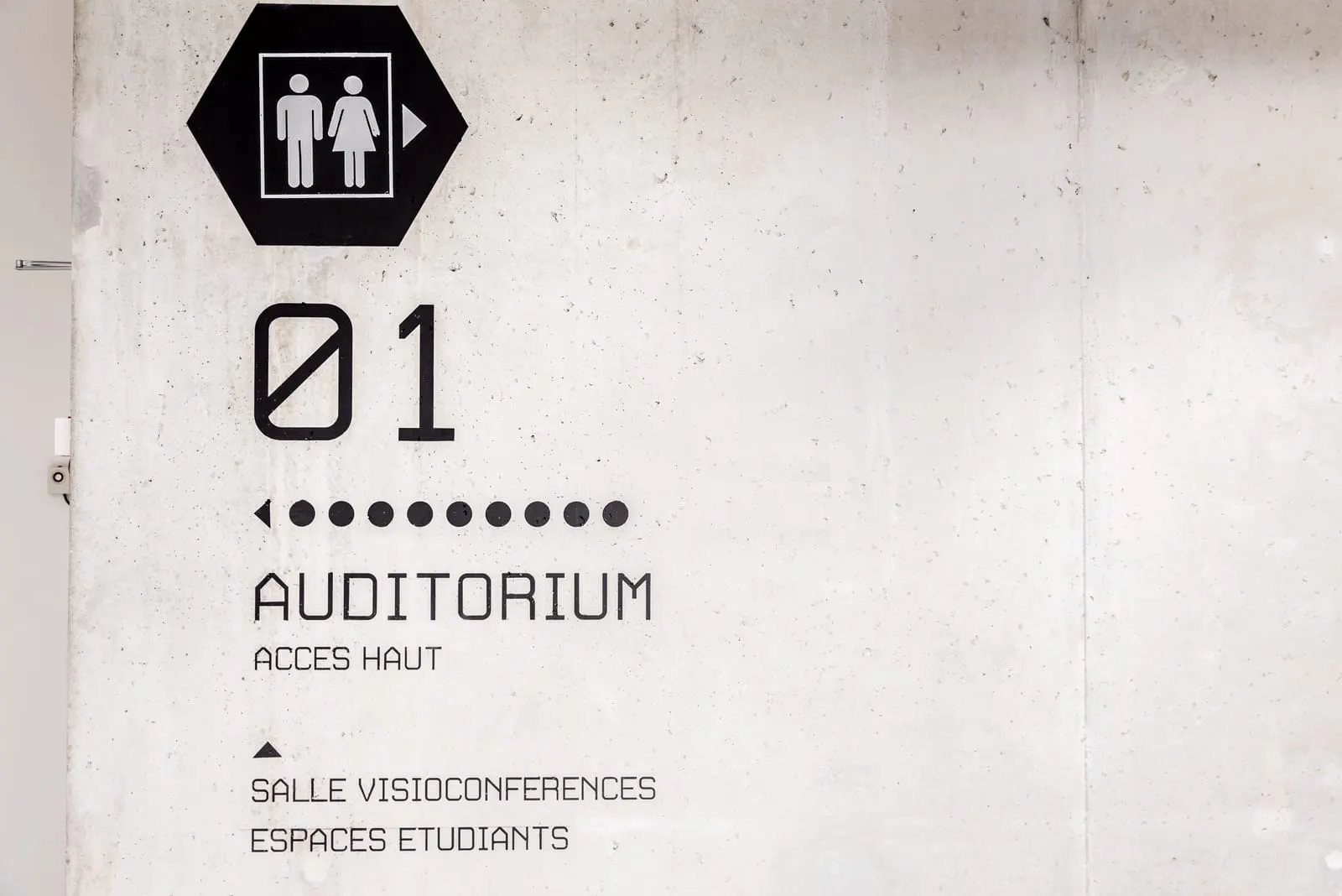 Panneau directionnel « Auditorium » appliqué sur un mur de béton brut
