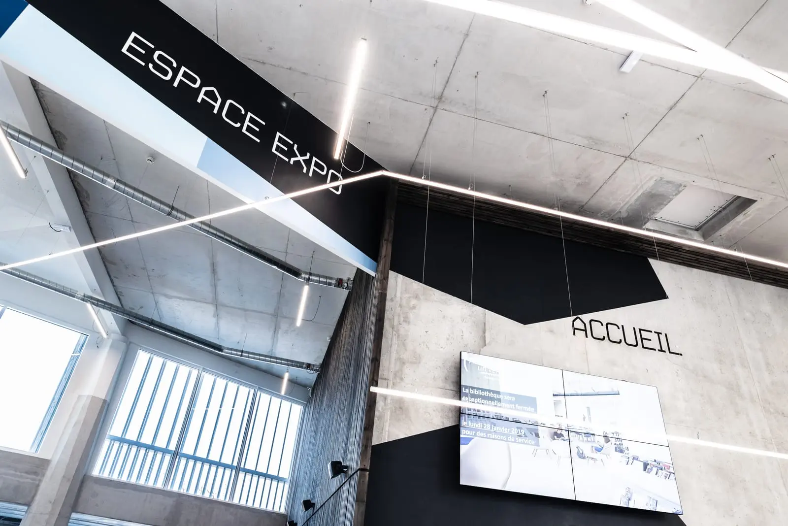 Lettrage « Espace expo » et filets lumineux sur un mur de béton