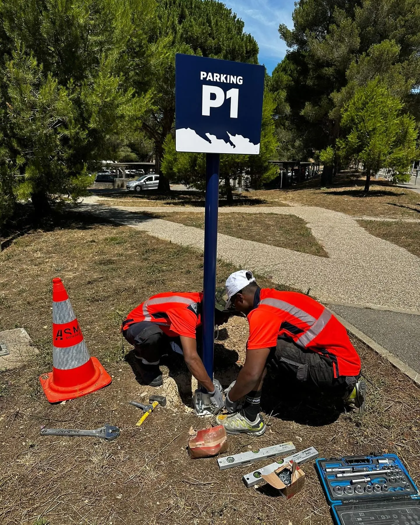 Salarié ASM scellant un mât de panneau au bord d’une voie, cône de protection posé