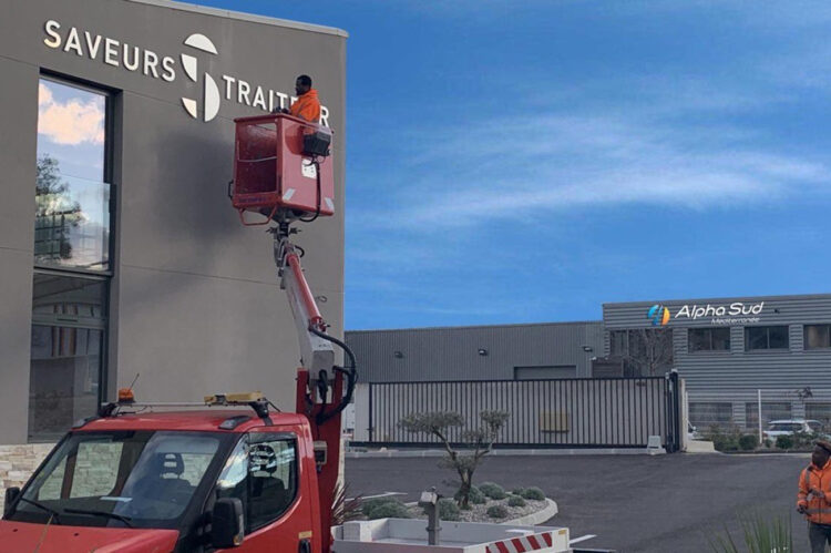 Installation de signalétique verticale sur mesure sur la façade d’un bâtiment par un technicien ASM.
