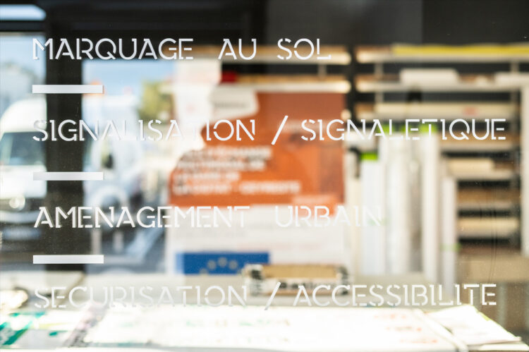 Vitrophanie adhésive blanche sur vitrine avec textes de signalétique intérieure et extérieure.
