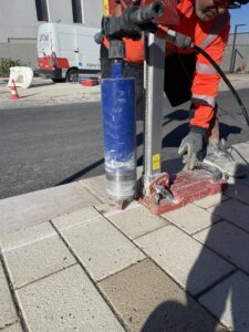 Technicien ASM utilisant une carotteuse pour préparer le sol avant la pose de potelets de sécurité urbains.