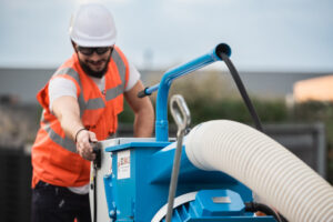 Ouvrier ASM en gilet orange préparant un sol avec une grenailleuse pour l’application de résine.