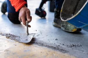 Technicien ASM effectuant une réparation de dallage avec mortier sur sol industriel.