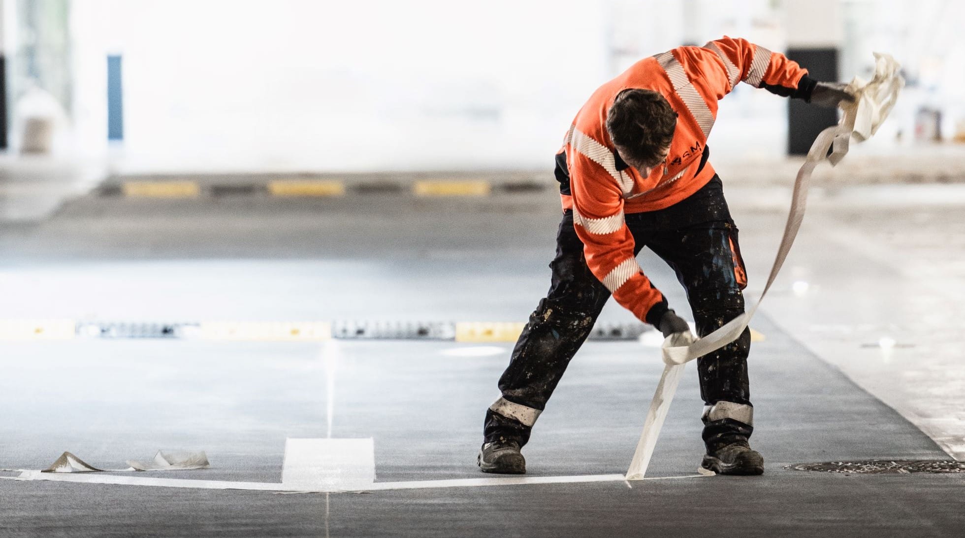 Technicien ASM appliquant un marquage au sol dans un parking couvert